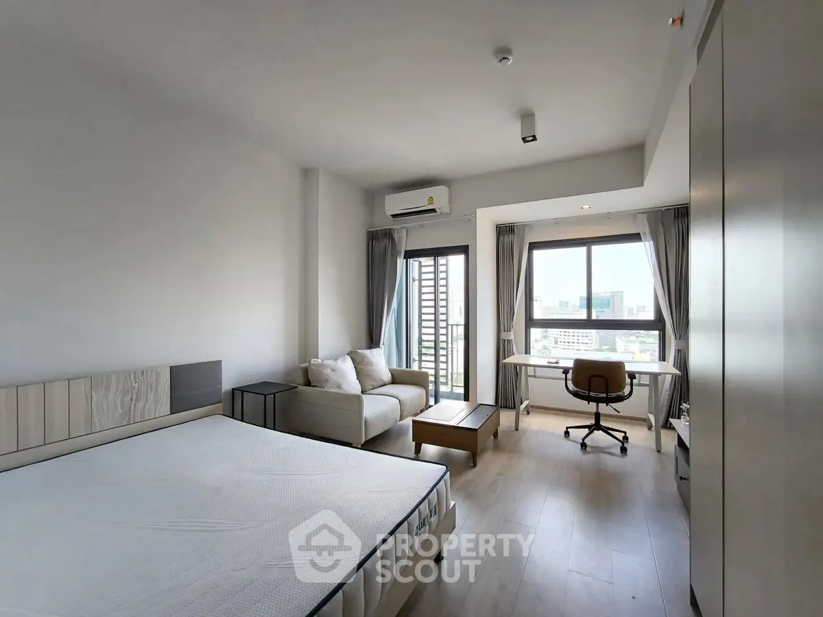 Spacious modern bedroom with city view, featuring a cozy seating area and work desk.