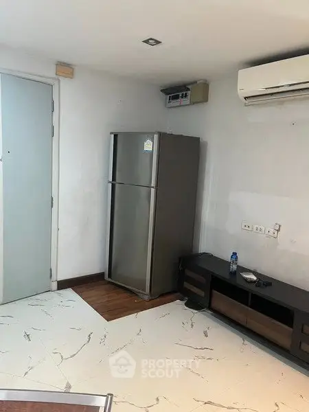 Modern apartment interior with sleek fridge and air conditioning unit, featuring stylish flooring and minimalist decor.