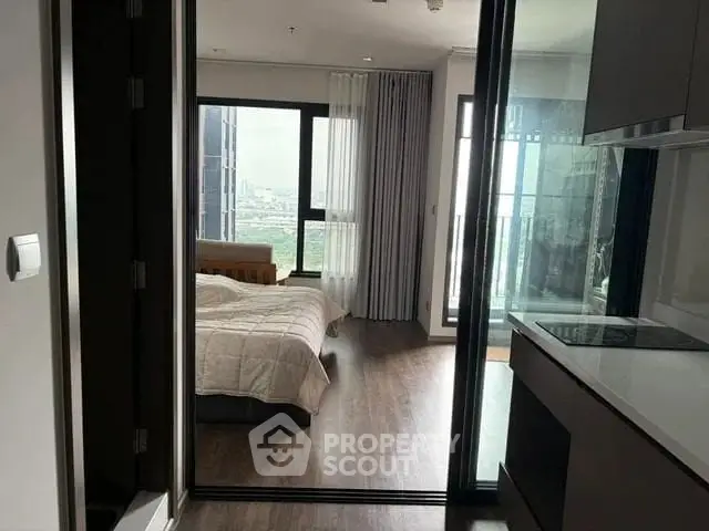 Modern apartment with bedroom and kitchen, featuring large windows and city view.