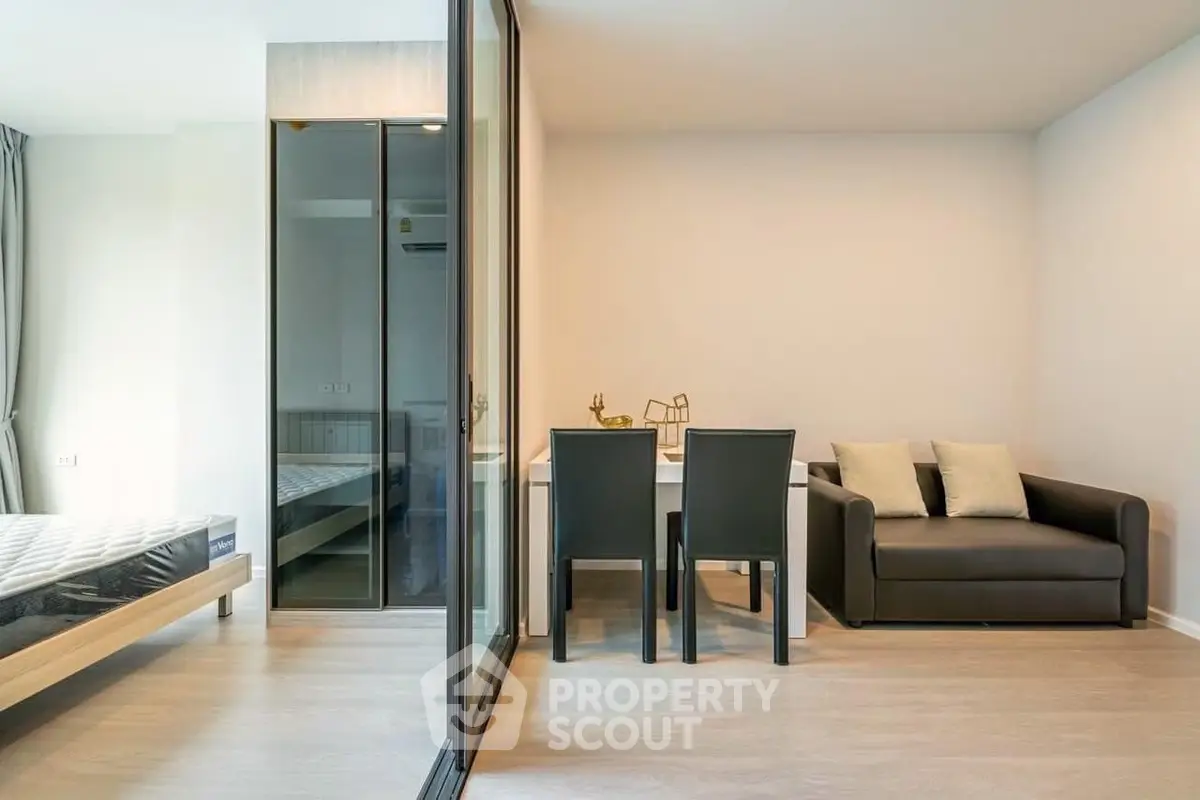 Modern studio apartment with glass partition, cozy seating, and dining area.