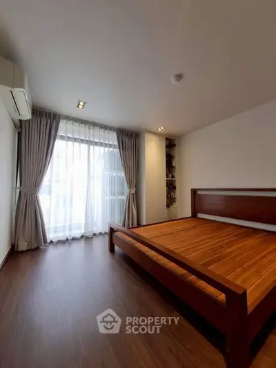 Spacious bedroom with wooden flooring and large window for natural light