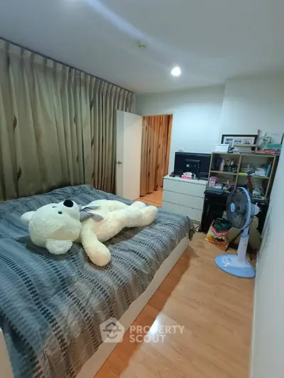 Cozy bedroom with wooden flooring, large teddy bear on bed, and organized shelving.