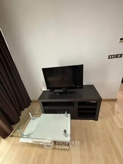 Modern living room with sleek TV stand and glass coffee table on wooden flooring.