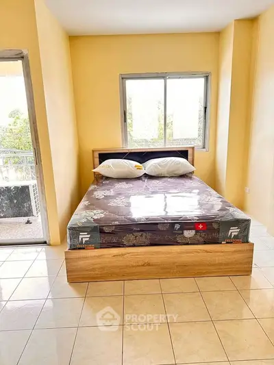 Bright bedroom with large window and balcony access, featuring a new bed with protective covering.