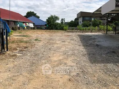 Spacious vacant land with potential for development, surrounded by greenery and nearby buildings.