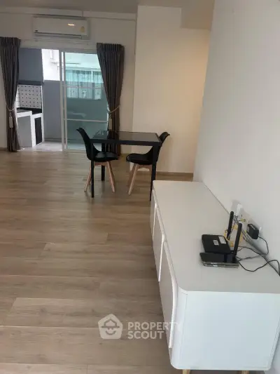 Modern living room with sleek furniture and wooden flooring, featuring a dining area and large windows.