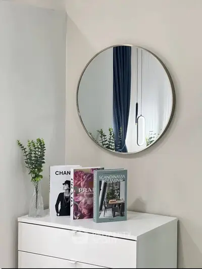 Stylish interior with round mirror and decor books on white dresser, perfect for modern living room.