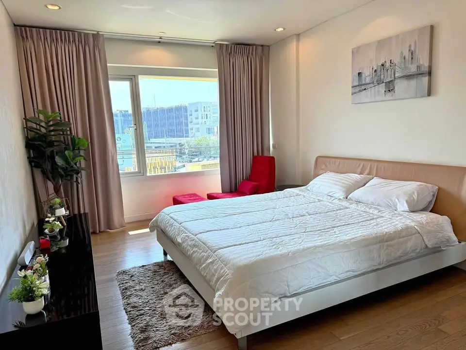 Spacious bedroom with modern decor and large window offering city views.
