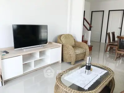 Spacious living room with modern TV setup and cozy wicker furniture.