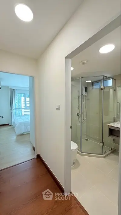 Modern apartment hallway leading to a bright bedroom and sleek bathroom with glass shower.