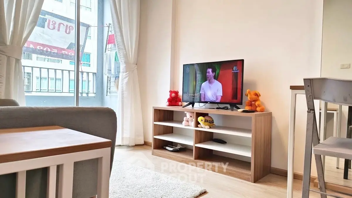 Modern living room with TV and plush toys, bright natural light from large window.