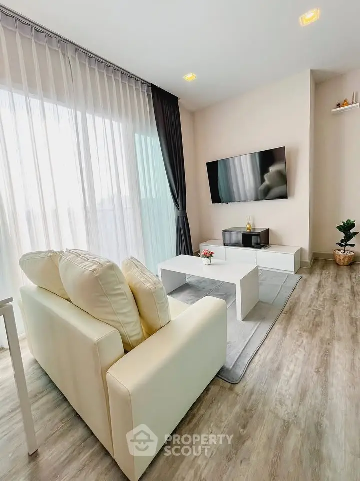 Modern living room with sleek furniture and large TV, featuring floor-to-ceiling windows and elegant decor.