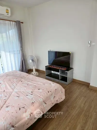 Cozy bedroom with floral bedding, TV, and natural light from large window.