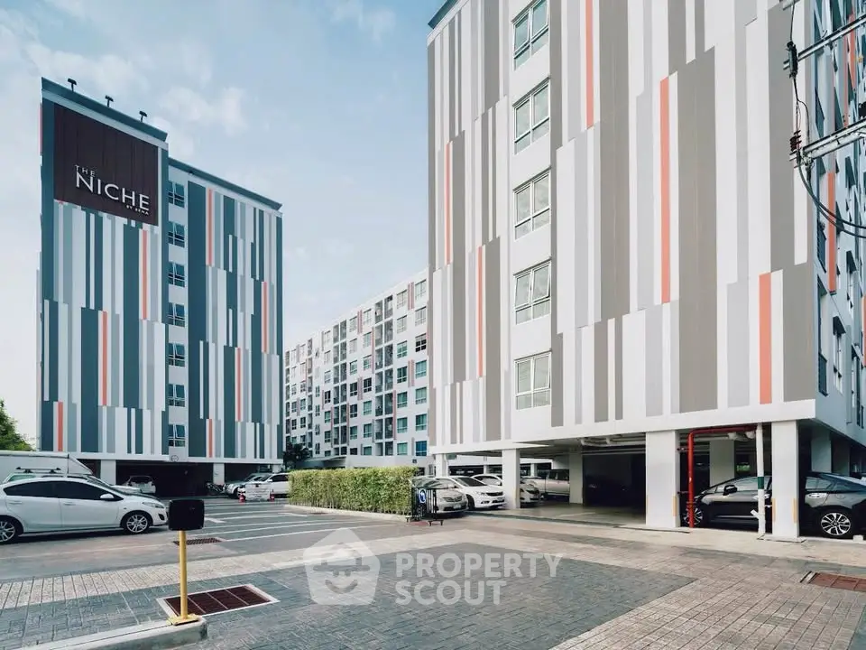 Modern apartment complex with stylish facade and ample parking space.