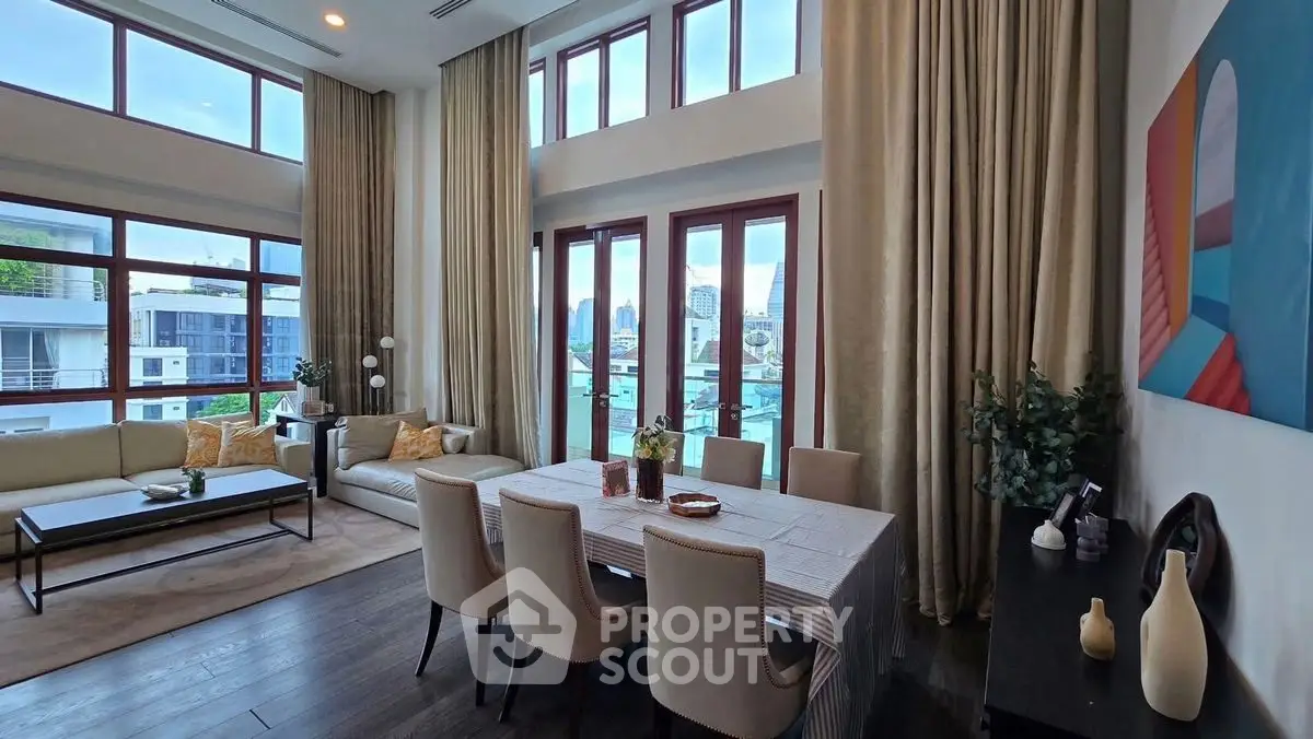 Luxurious living room with high ceilings and elegant dining area, featuring large windows and modern decor.