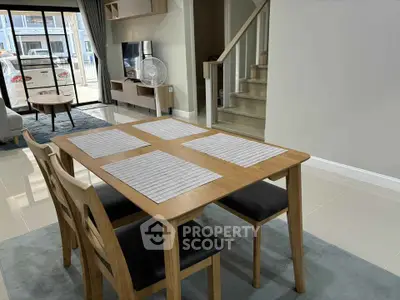 Modern dining area with wooden table and chairs, open layout leading to living room and staircase.