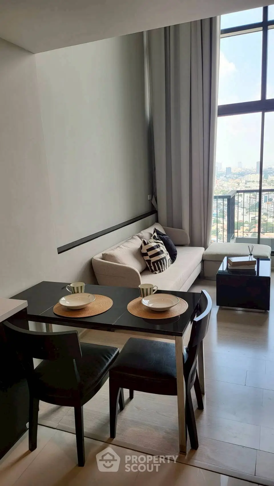 Modern living room with dining area and city view, featuring sleek furniture and large windows.