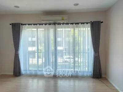 Bright living room with large window and elegant curtains, featuring a modern air conditioning unit.