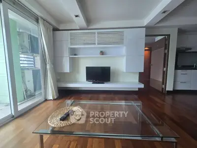 Modern living room with wooden flooring, glass coffee table, and built-in TV unit, offering a stylish and cozy ambiance.