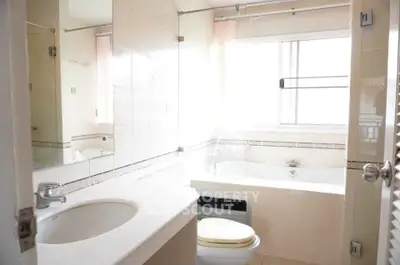 Bright bathroom with large window and bathtub, featuring modern fixtures and neutral tiles.