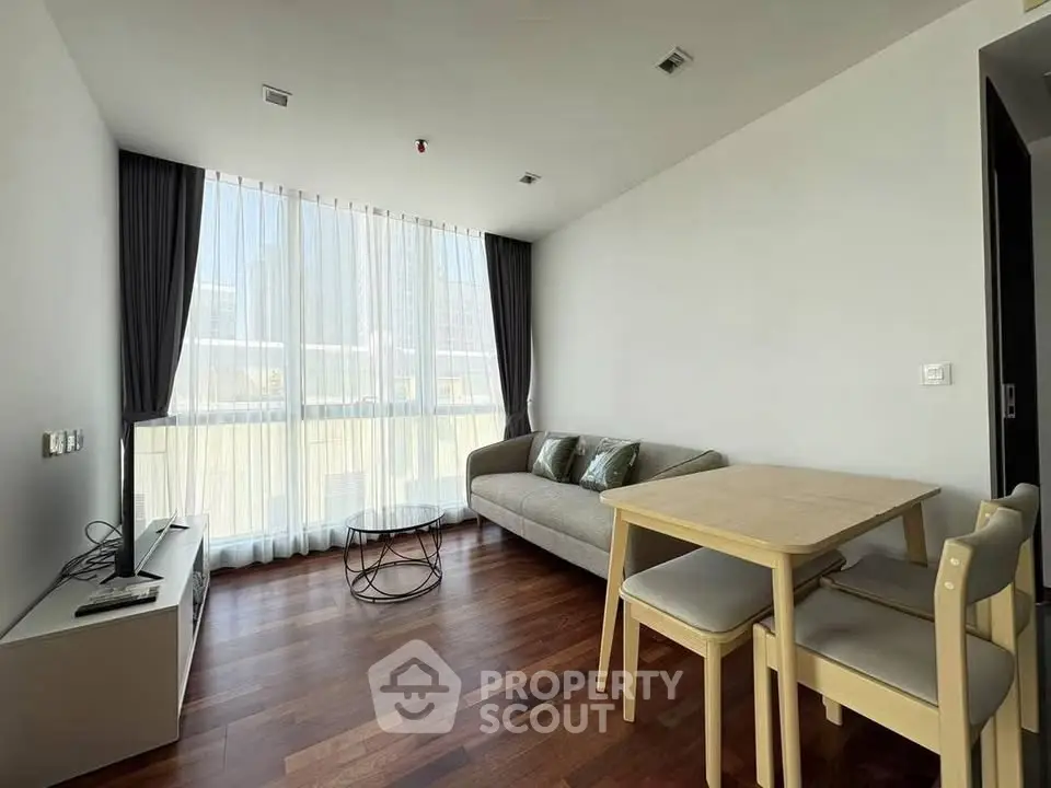 Modern living room with large window, wooden flooring, and minimalist furniture in a bright apartment.