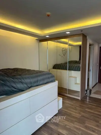 Modern bedroom with elevated bed and mirrored wardrobe in stylish apartment.