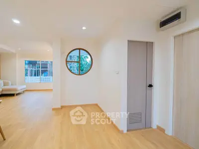 Spacious modern living room with wooden flooring and unique round window design.