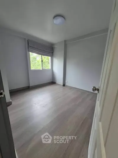 Spacious empty bedroom with large window and wooden flooring