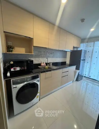 Modern kitchen with sleek cabinetry, washing machine, and large window for natural light.
