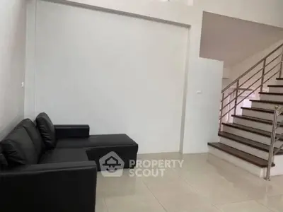 Spacious modern living room with sleek black sofa and elegant staircase.