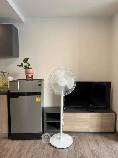 Modern living room with sleek fridge, TV, and stylish fan in a cozy apartment setting.