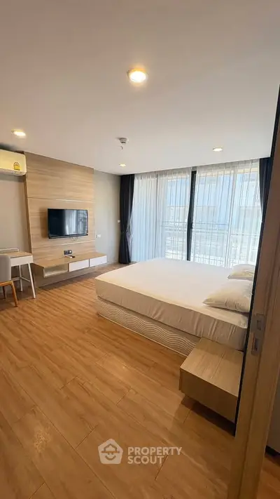 Modern bedroom with wooden flooring and large windows offering natural light.