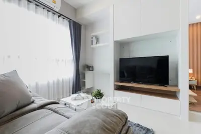 Modern living room with sleek furniture and large TV, featuring natural light and stylish decor.