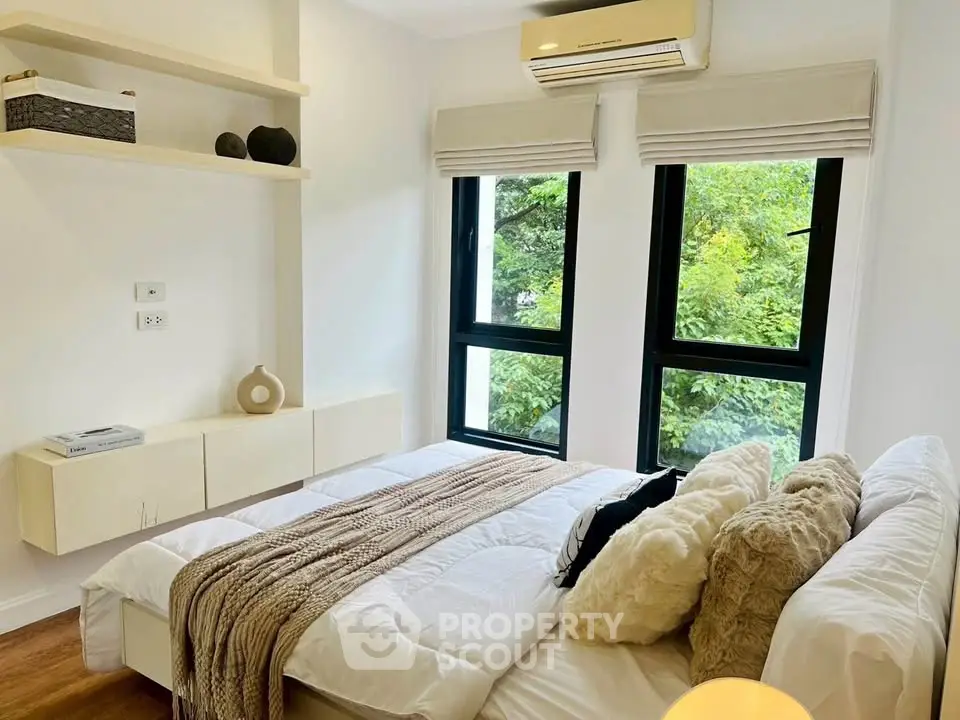 Cozy bedroom with large windows and modern decor, featuring lush greenery views.