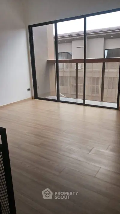 Spacious modern living room with large windows and wooden flooring, offering ample natural light.