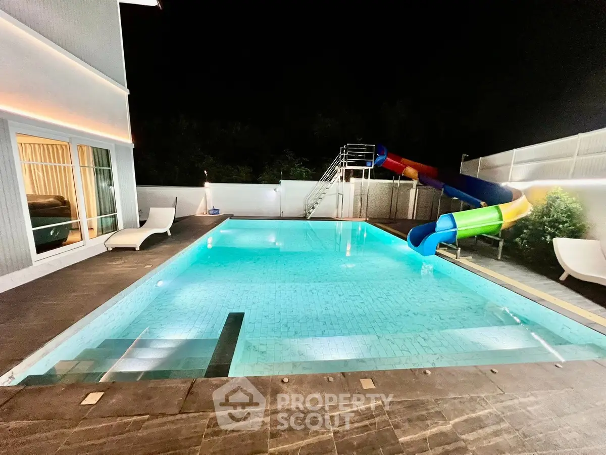 Luxurious night view of a private pool with water slide and elegant poolside seating.