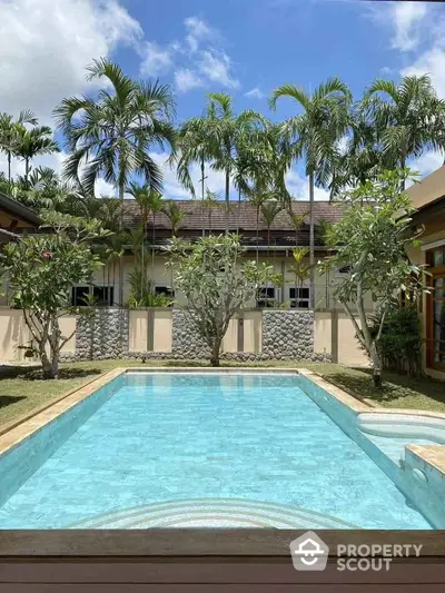 Stunning backyard pool with lush tropical landscaping and clear blue skies.