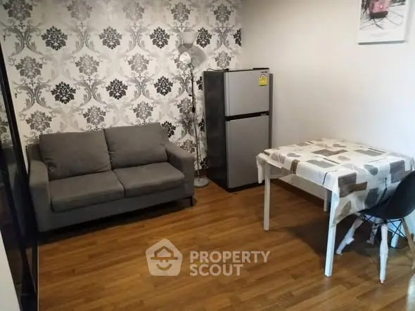 Cozy living room with modern decor, featuring a gray sofa, patterned wallpaper, and compact dining area.