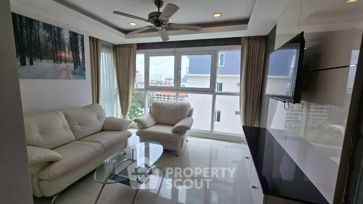 Modern living room with large windows and white leather furniture in a high-rise apartment.