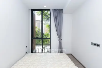 Modern bedroom with large window and elegant curtains, offering a serene view of greenery.