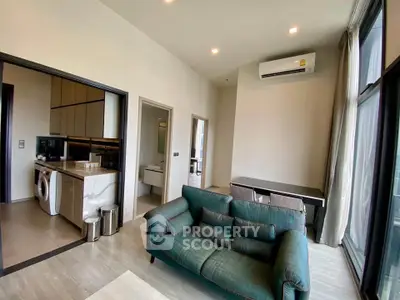 Modern living room with green sofa, open kitchen, and large windows in a stylish apartment.
