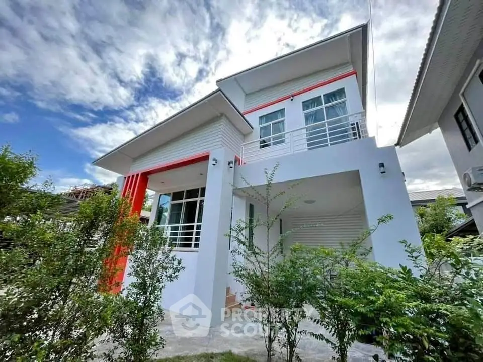 Modern two-story house with red accents and lush greenery under a bright blue sky.