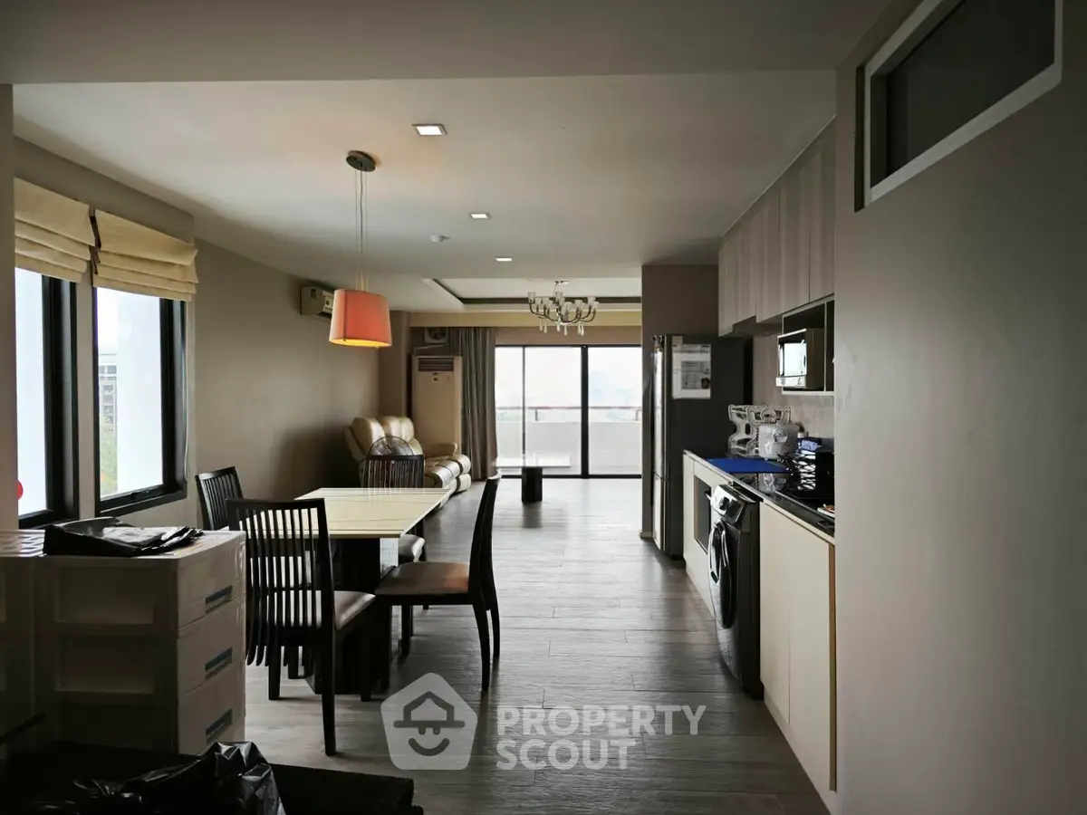 Spacious modern living room with dining area and balcony view, featuring sleek furniture and natural light.