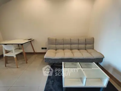 Cozy living room with modern sofa, glass coffee table, and study desk in a bright apartment.