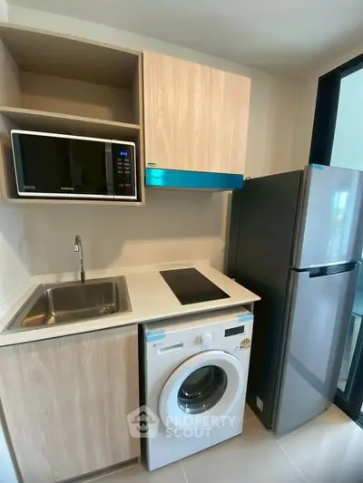 Modern compact kitchen with appliances including washing machine, microwave, and fridge in a sleek design.