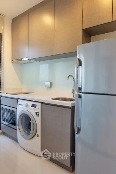 Modern kitchen with sleek cabinets, washing machine, and stainless steel fridge.