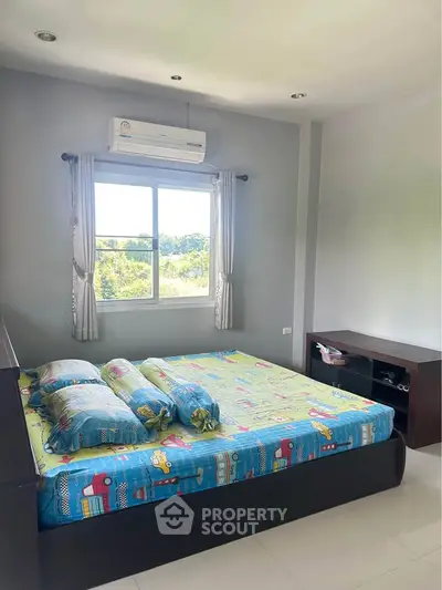 Bright bedroom with large window and air conditioning, offering a serene view of greenery.