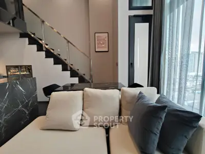 Modern living room with elegant staircase and large windows offering city views.