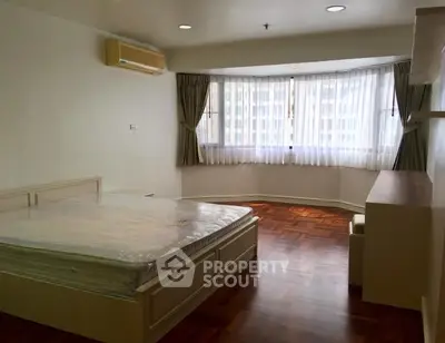 Spacious bedroom with large windows and wooden flooring in modern apartment.