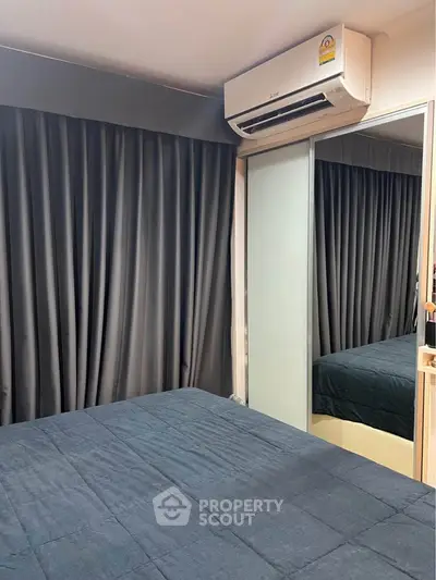 Cozy bedroom with mirrored closet and air conditioning unit, featuring dark curtains and bedding.